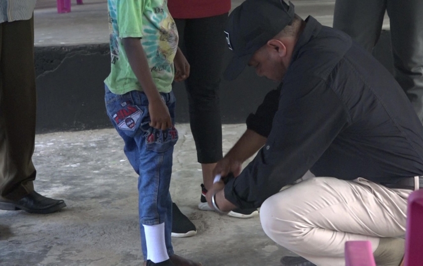 Dr. Filep Wamafma saat menyerahkan bantuan kaoskaki dan sepatu, sekaligus langsung memakaikannya pada kaki seorang siswa