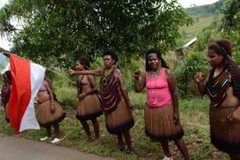 Perempuan Papua mengenakan busana tradisional dan mengibarkan Bendera Merah Putih saat menyambut kedatangan Presiden Joko Widodo dan rombongan di Jayapura, Papua, 9 Mei 2015. [Foto: AFP PHOTO / ROMEO GACAD]